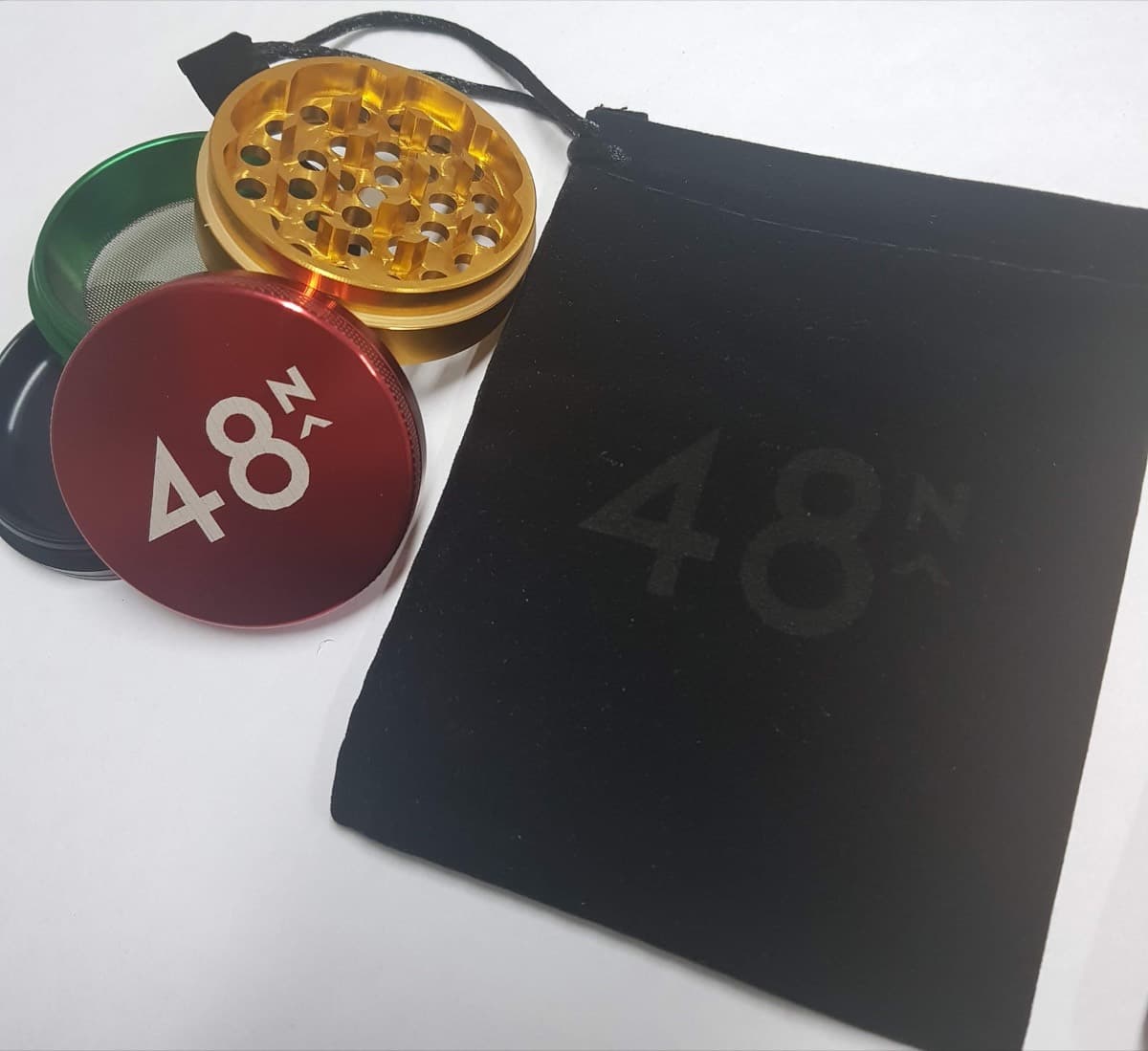 Red, gold and green 4-part grinder printed with the 48 North logo, beside a matching branded pouch