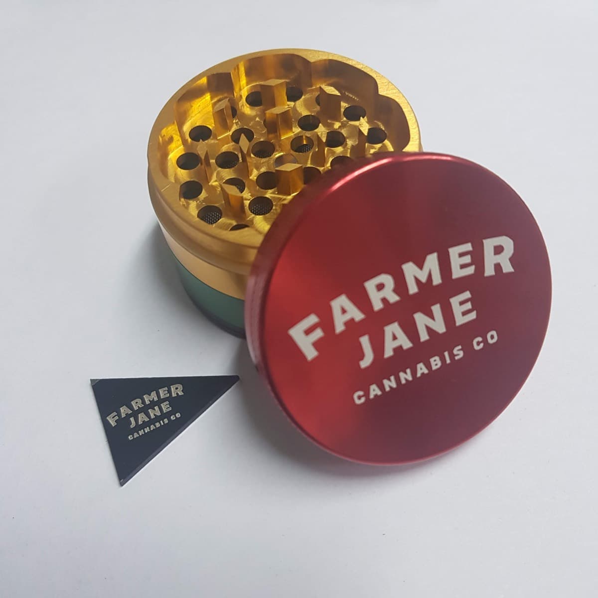 Multi-colour 4-part grinder with a red printed lid and gold teeth chamber, with a matching Farmer Jane scraper